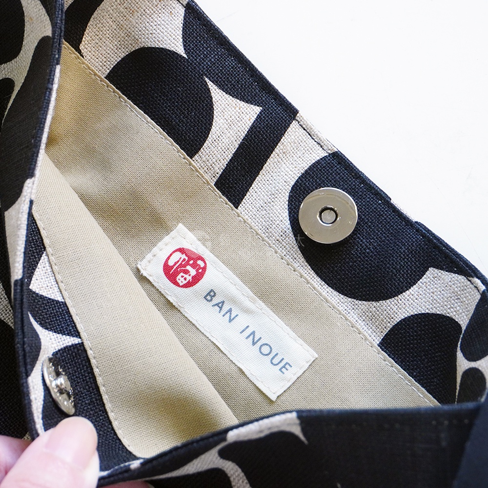 BAN INOUE 標籤縫製於自然織紋麻布斜背包內部，斜背包印有黑色果實花紋。
