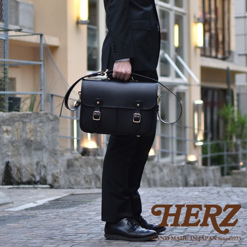 黑色皮革雙肩包，配有金色釦環和可調節肩帶，由男子在戶外展示。