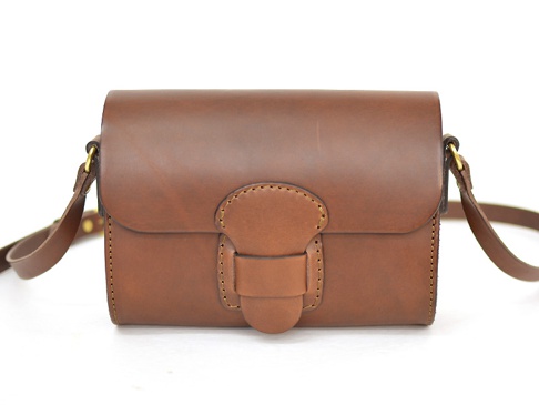 職人手作皮革寬扣帶馬鞍包，採用深棕色皮革製成，正面有寬版皮革扣帶和圓潤的縫線設計，搭配金色金屬扣件和可調式皮革背帶。