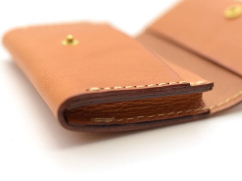 職人手作的經典名片收納夾，採用淺棕色皮革製成，以白色縫線手工縫製，設有金色按扣。