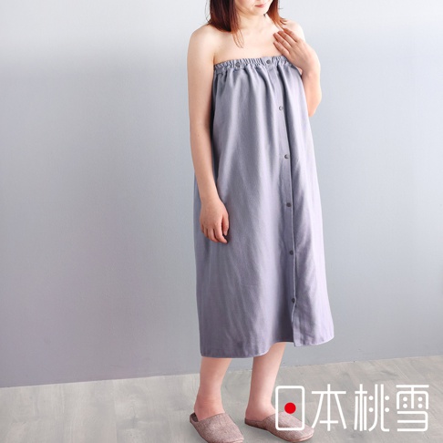 一位女性穿著灰色棉紗混紡平口鬆緊浴裙，浴裙有鈕扣設計，長度及膝，搭配室內拖鞋。