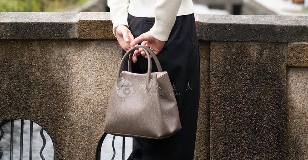 皮革手提托特包，採用簡約的梯形設計，搭配雙提把，顏色為大地色系。