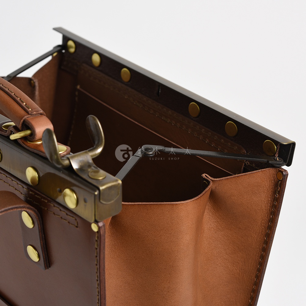棕色皮革復古口金後背包，展示內部結構與金屬鎖扣細節，皮革質地光滑，帶有復古黃銅色五金配件，強調職人手作質感。