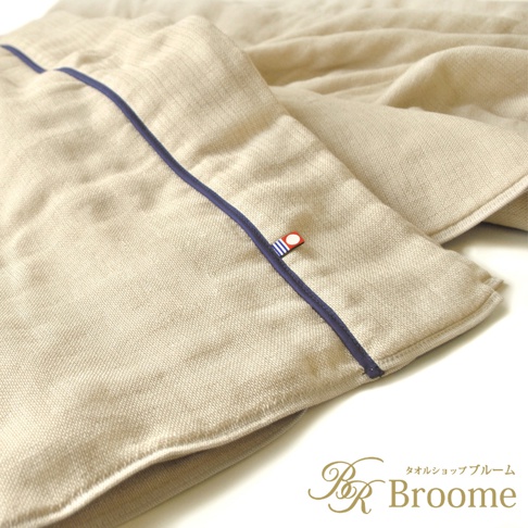 米色五層紗四季被，表面有細緻紋理，邊緣滾有深藍色滾邊，並有一個帶有紅、藍、白色條紋的小標籤。