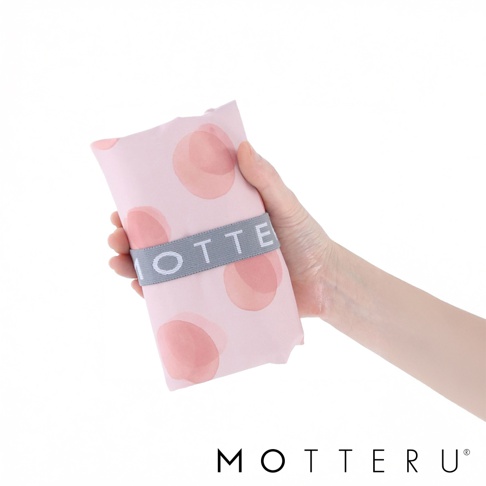 手持粉色圓點圖案的摺疊保冷托特袋，由織物製成，由灰色束帶固定，束帶上有白色「MOTTERU」字樣。