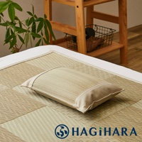 藺草調濕透氣舒眠枕，枕面為淺褐色藺草編織，枕套邊緣為米白色布料，擺放在同款淺褐色藺草編織的床墊上。