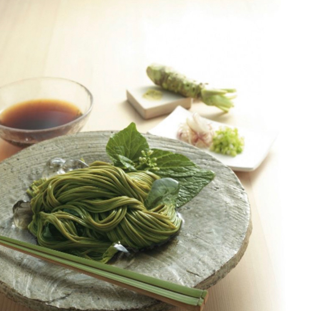 一盤綠色的蕎麥麵，搭配新鮮的芥末、蔥花、薑末，以及一碗醬汁，旁邊有兩根竹筷。