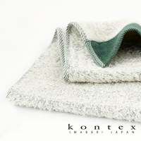 一條對折的淺灰色長纖有機棉毛巾，邊緣飾有綠色人字紋織帶，質感柔軟蓬鬆。