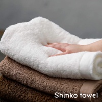 MAISON BLANC 輕奢柔膚匹馬棉毛巾，堆疊展示，頂部為白色，中間為淺棕色，底部為深棕色。一隻手輕柔地觸碰白色毛巾，展現其柔軟質感。