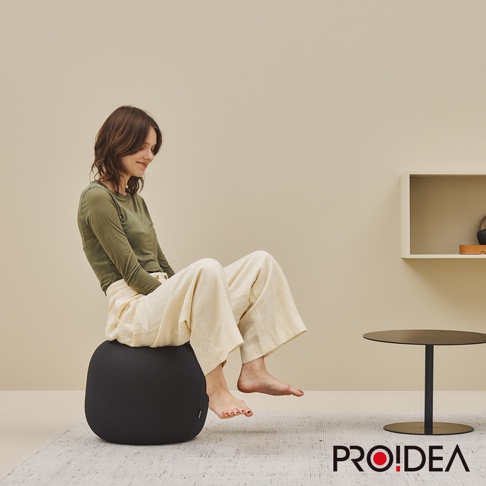 一位女性坐在黑色的MALLOW Knit收納彈力平衡球-迷你款上。此款平衡球採用針織材質，外形圓潤，底部有品牌標示。