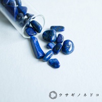 試管瓶中及瓶外散落著多顆深藍色、帶有金色斑點的拋光礦石，部分呈現塊狀，部分為鵝卵石狀。