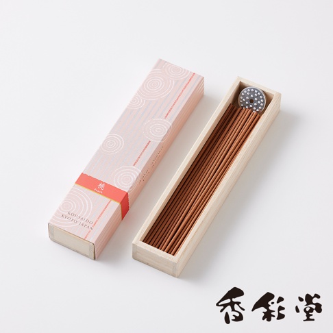 一盒粉色帶有白色螺旋圖案的長方形紙盒，盒蓋旁是裝有許多淺褐色細長線香的淺色木盒，木盒內有一個銀色圓形香座。