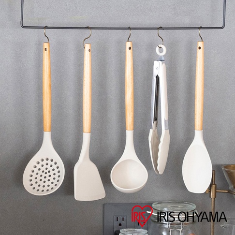 一套白色矽膠廚房用具，包含漏勺、鍋鏟、湯勺、夾子和煎匙，皆配有淺木色手柄，懸掛於黑色掛架上。