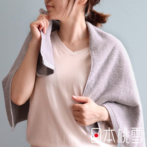 一名女子披著一條淺灰色精梳棉毛巾，毛巾觸感柔軟，邊緣有精緻的織紋。