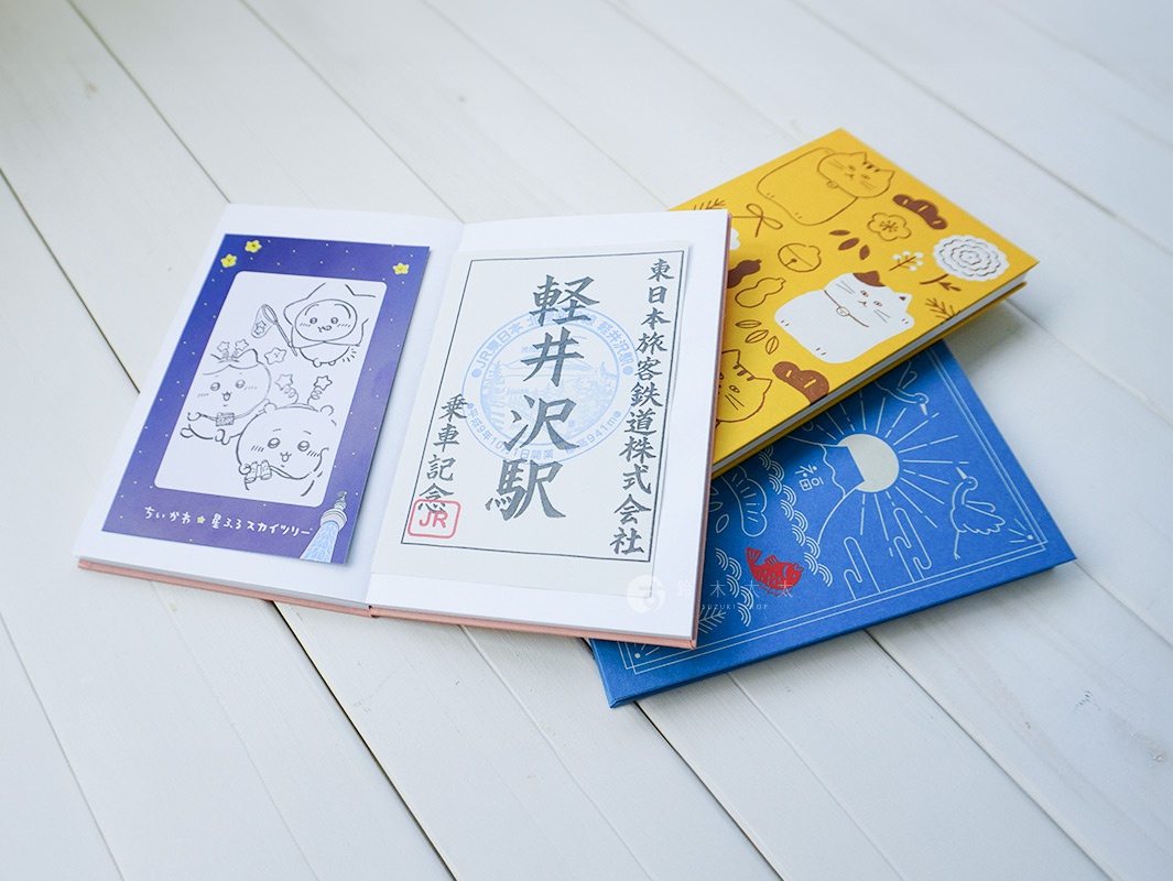 三本美濃和紙御朱印帳，分別為粉色封面內頁印有可愛卡通圖案、白色內頁印有日文車站戳記、以及黃色封面印有貓咪圖案和藍色封面印有日式吉祥圖案。