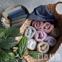 兩個藤編籃子裡裝有不同顏色的精梳棉飯店浴巾，包括藍色、灰色、粉色、紫色和米色。其中一個籃子裡疊放著數條深淺不一的藍灰色浴巾，旁邊還有一個木質沐浴刷和圓形肥皂。另一個籃子裡則捲成圓筒狀擺放著多條淺色系的浴巾，如白色、淺灰、淺粉、淺紫和淺棕色。