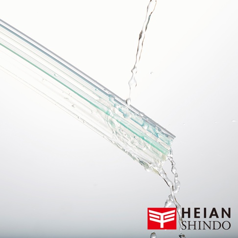 透明的家具防倒固定墊，帶有綠色條紋，表面有水流過，呈現濕潤狀態。