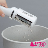 白色免耗材抗菌衣物除塵刷，前端的滾輪上沾有灰白色棉絮，正被傾斜置於一個淺灰色的圓形容器上方，容器內散落著少量棉絮。