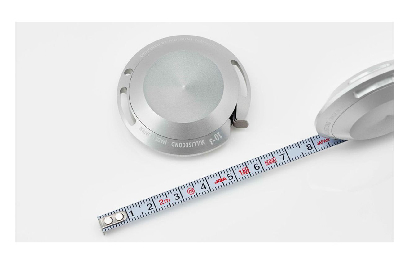銀色鋁製卷尺，2公尺長，帶有公分和英吋刻度。卷尺主體為圓形，上方刻有「DESIGNED BY HIDEBUMI YAMAMOTO」及「MADE IN JAPAN」字樣。