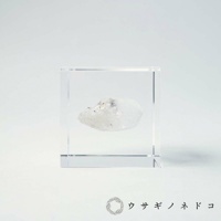 透明立方體水晶塊中，封存著一塊白色半透明的礦石，部分區域帶有淡紫色或灰色雜質，礦石表面呈現天然晶體結構。