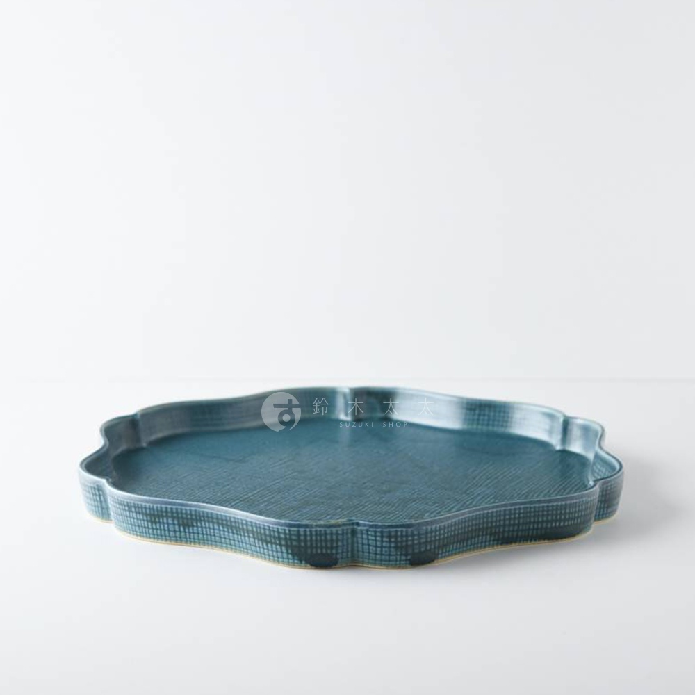 藍綠色美濃燒花型甜點盤，表面帶有細緻紋理與網格狀藍色線條，盤邊為不規則的花瓣狀，盤底露出陶土原色。
