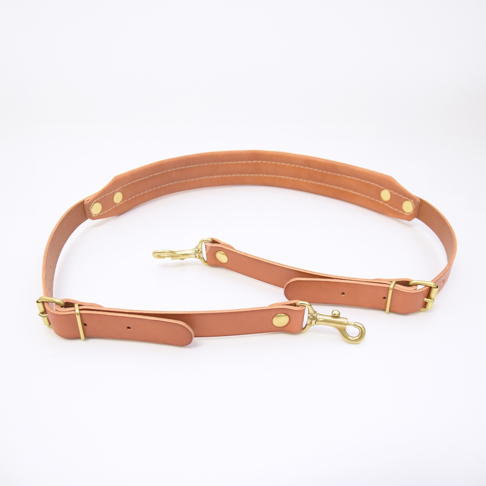 職人手作皮革加厚減壓肩背帶，呈現自然的棕褐色，搭配古銅色金屬扣環與掛鉤，皮革表面平整，車縫線清晰，設計簡約實用。