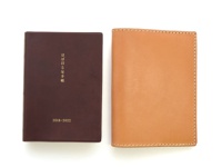 深棕色皮革書套，表面有金色日文文字「ほぼ日 5年手帳」及「2018-2022」字樣。右側為淺棕色皮革書套，邊緣有白色縫線。