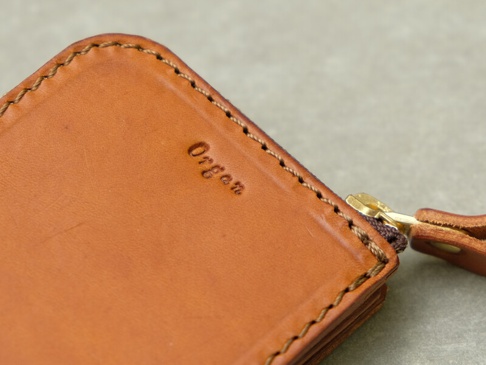 職人手作皮革Organ全包式拉鍊卡片鑰匙包，以柔軟的淺棕色皮革製成，車縫線為深咖啡色，右側有金色拉鍊及同色系皮革拉頭，皮革表面壓印有「Organ」字樣。