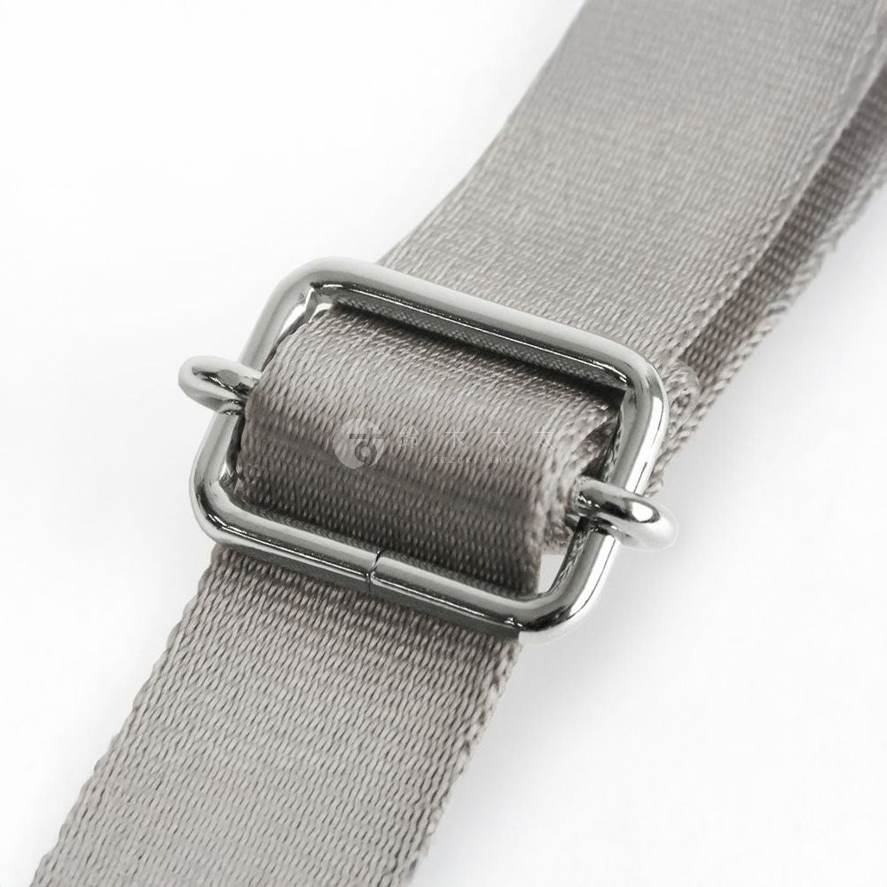一個銀色金屬帶扣通過一條灰色的尼龍斜背包肩帶，靠近拍攝。