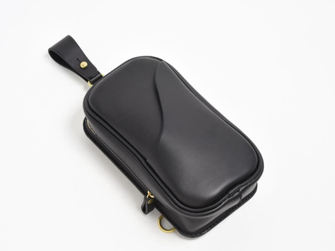 黑色皮革直立型斜背包，頂部有手提帶，側邊有拉鍊和金屬環。