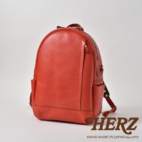 紅色職人手作皮革多功能後背包，圓潤飽滿的包身設計，帶有金屬拉鍊和側邊收納口袋，整體呈現簡約大方的風格。