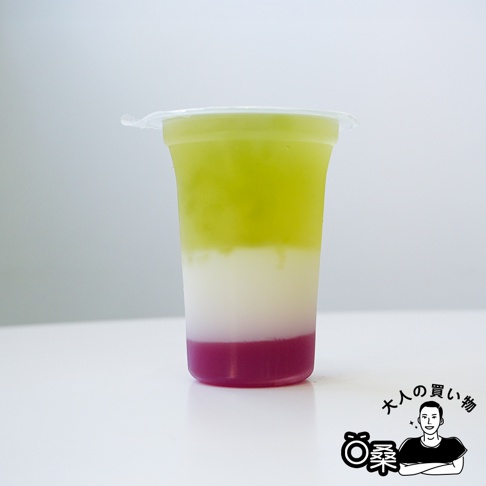 透明塑膠杯裝著三層漸層飲品，由上至下分別是淡綠色、白色和紫紅色。杯口覆蓋透明塑膠封膜。