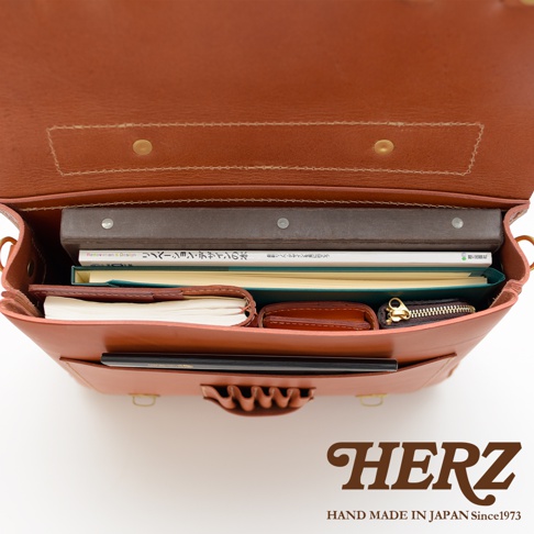 職人手作皮革傳統歐風三用學生包，棕色皮革，包內可見兩本書、筆記本、錢包和拉鍊小包，結構緊湊。