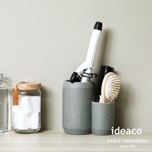 一高一低兩個灰色砂岩材質的收納筒，較高的收納筒內有一個白色電捲棒，較矮的收納筒內有一支木柄梳子和一支黑色圓筒梳。