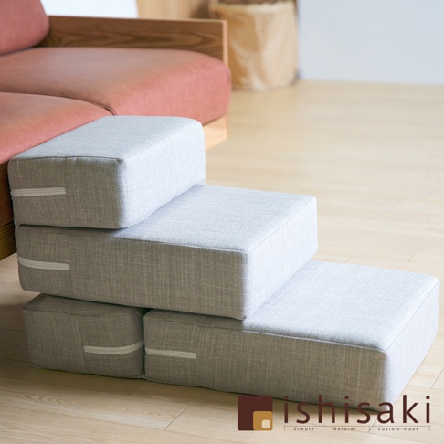 淺灰色織物材質的可折疊寵物樓梯，共三層，堆疊在木質地板上，旁邊是紅色布藝沙發。