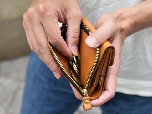 雙手正在打開一個棕色皮革方形短夾，展示內部的拉鍊零錢袋，裡面裝有硬幣，拉鍊為金色。
