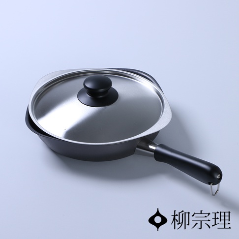 柳宗理品牌的雙網紋單手鐵鍋，主體為黑色鑄鐵材質，配有圓形不鏽鋼鍋蓋，鍋蓋中央設有黑色圓形把手，鍋身側邊連接黑色圓柱狀長握柄，柄端帶有金屬掛環，整體造型簡約洗練，以淺灰色為背景，右下角印有柳宗理品牌標誌。