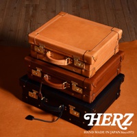 職人手作皮革英倫風便攜手提行李箱，堆疊擺放。最上方為淺棕色皮革，中間為中棕色皮革，最下方為黑色皮革。三只行李箱均有金屬鎖扣、皮革提把及金屬角飾。