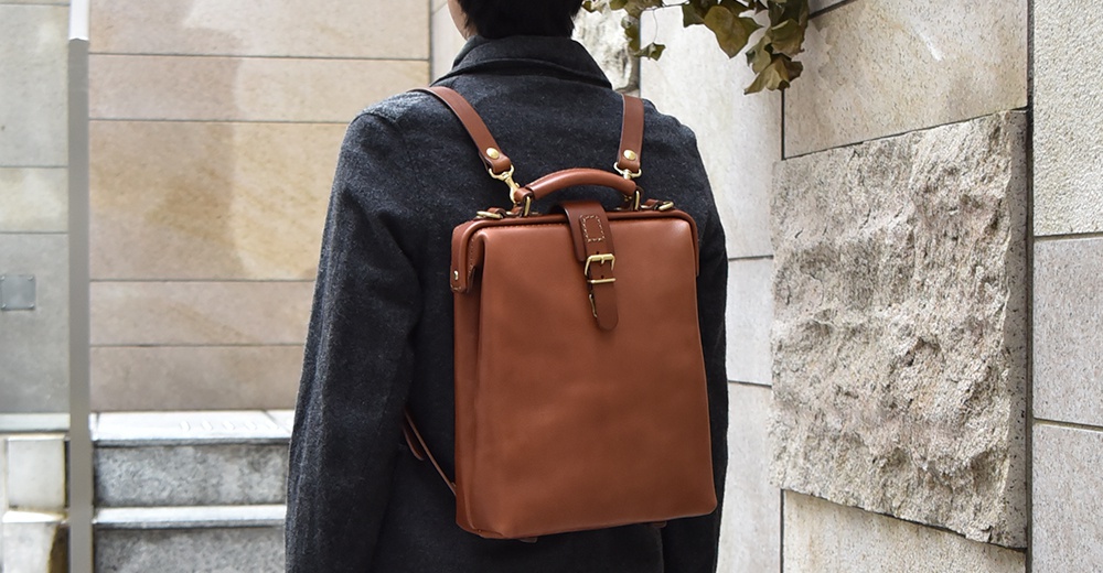 棕色皮革軟式杜勒斯包，附有金屬扣和可調節肩帶，由一人背於背部。