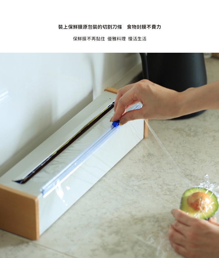 日本製原木鋼製保鮮膜切割器，白色主體搭配原木邊框，內嵌金屬切割條，使用者正用藍色滑蓋切割保鮮膜，準備包裹半顆酪梨。
