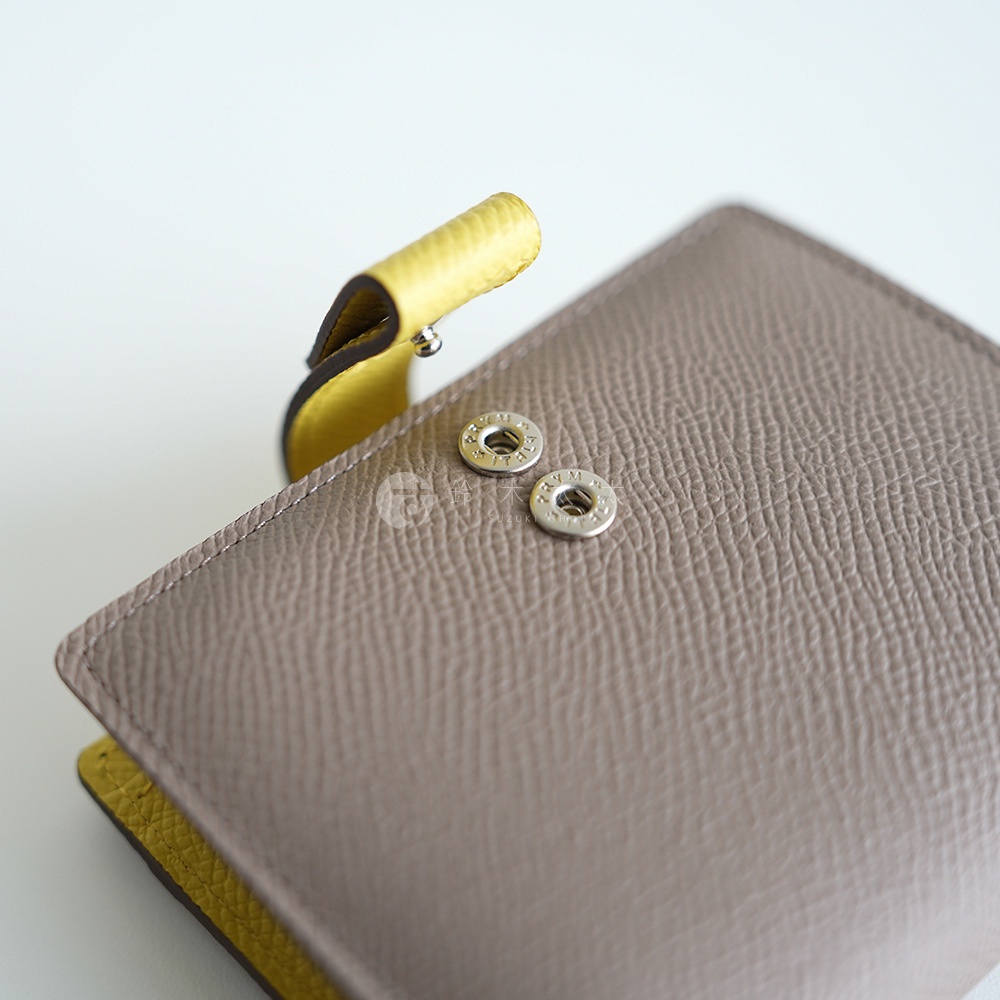 Atelier nuu 淺棕色雙折短夾，有黃色內襯和銀色金屬按扣，細節處可見品牌標識