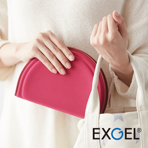 女性手持桃紅色半圓形坐墊，坐墊邊緣為深紅色，置於白色帆布袋旁。