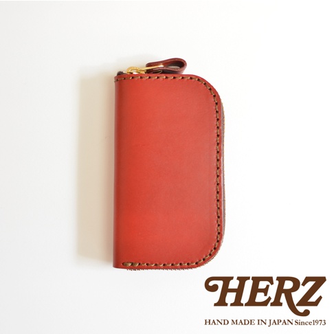 職人手作皮革橢圓形拉鍊鑰匙包，紅色，附有金色拉鍊和品牌標誌。