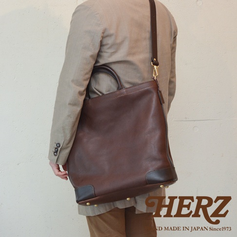 模式B： 日本HERZ職人手作皮革Organ兩用拉鍊托特包 G-45，採用棕色皮革製作，有頂部提把與可拆卸肩帶，包款底部有深色皮革加固和金屬腳釘。