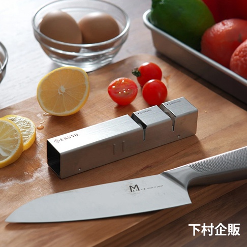 ESSYO 越匠系列可拆式不鏽鋼雙滾輪磨刀器，銀色不鏽鋼材質，設有「1. Diamond」和「2. Ceramic」兩段式磨刀槽。背景有檸檬、小番茄、雞蛋和刀具。