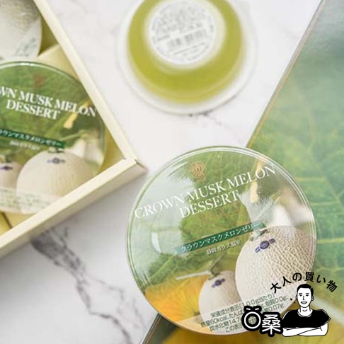 靜岡頂級皇冠哈密瓜果凍禮盒，內有數個透明圓形果凍，果凍內可見哈密瓜圖案與綠色果凍。部分果凍盒蓋印有「CROWN MUSK MELON DESSERT」字樣，另有日文說明。禮盒為淺黃色紙盒。