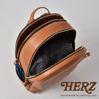 棕色皮革多功能後背包 R-21，主隔層敞開，露出內部黑色的收納袋。側面有一個小口袋，裝有藍色圖案的物品。背包配有金色拉鍊和皮革提把。