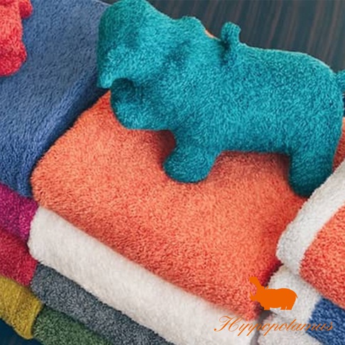 藍綠色竹棉混紡河馬造型抓握玩偶，疊放在橙色、白色、藍色、紅色、綠色等多色毛巾上方。