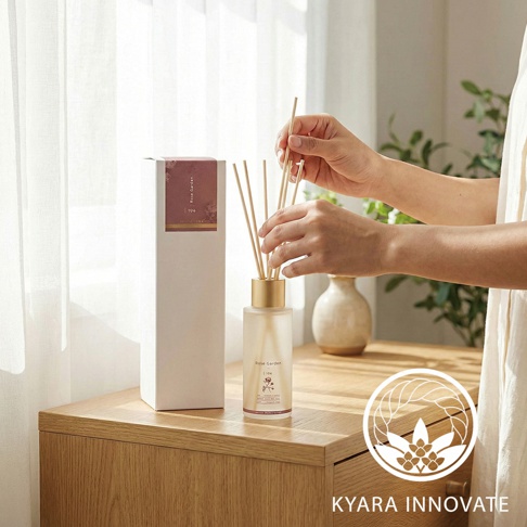 KYARA INNOVATE 室內擴香竹，手部正在將擴香竹插入玻璃瓶中，背景是明亮的窗簾和家具。