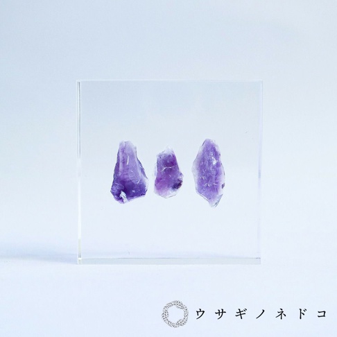 透明方形壓克力磚中，嵌入三塊不規則形狀、深淺不一的紫色紫水晶切片標本。